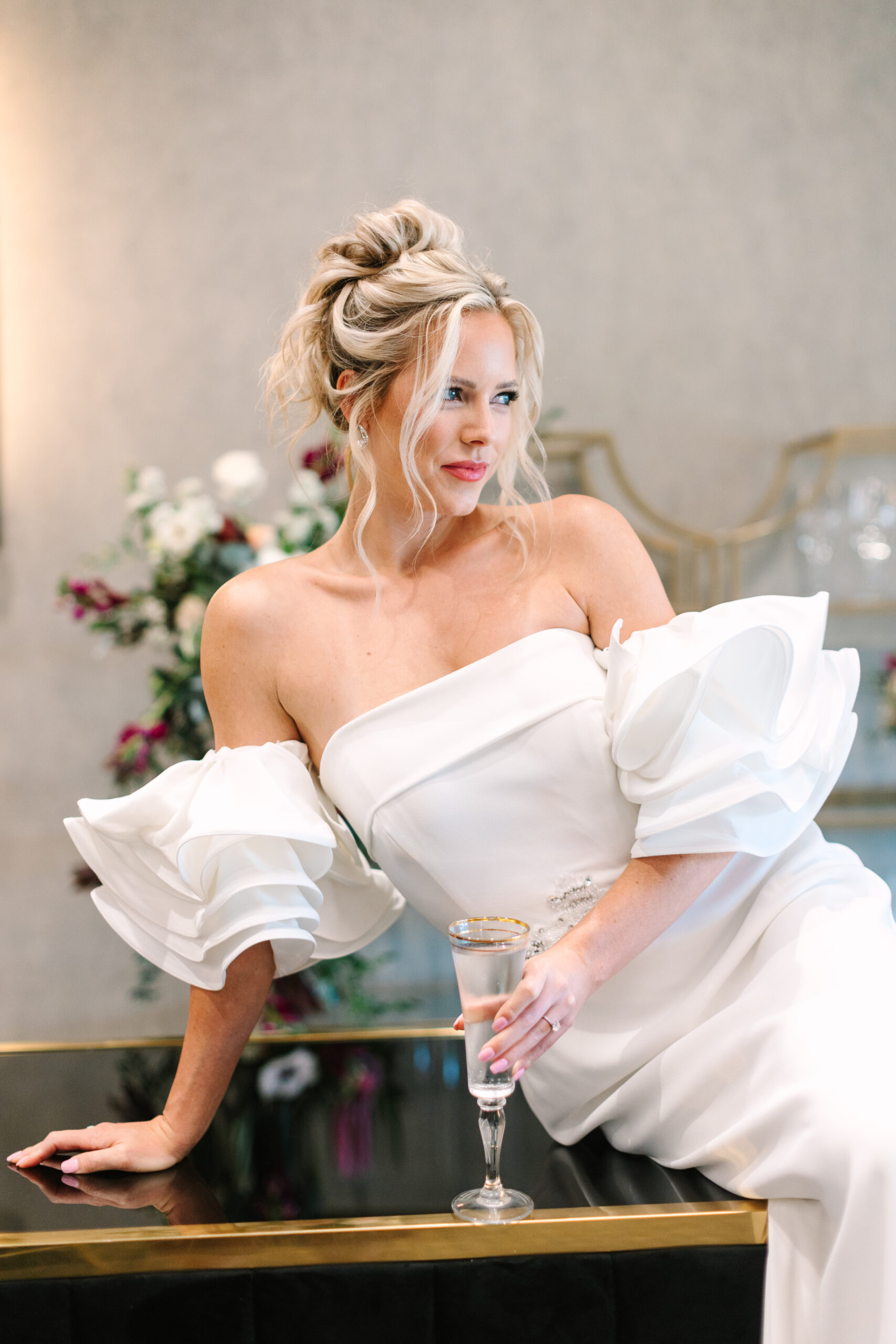 Bride sitting on a bar, in her gown with a glass of champagne